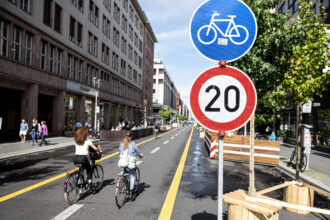 Two cyclists ride on the car-free section of Friedrichstraße in Berlin, where a speed limit of 20 kilometers per hour (12 mph) applies. Credit: Fabian Sommer/picture alliance via Getty Images