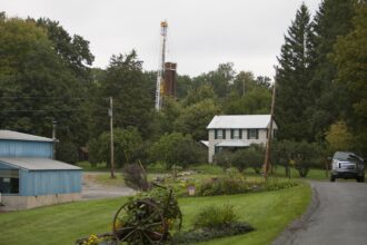 A car drives by a home with a nearby derrick drilling for natural gas near Calvert, Pennsylvania. Credit: Robert Nickelsberg/Getty Images.