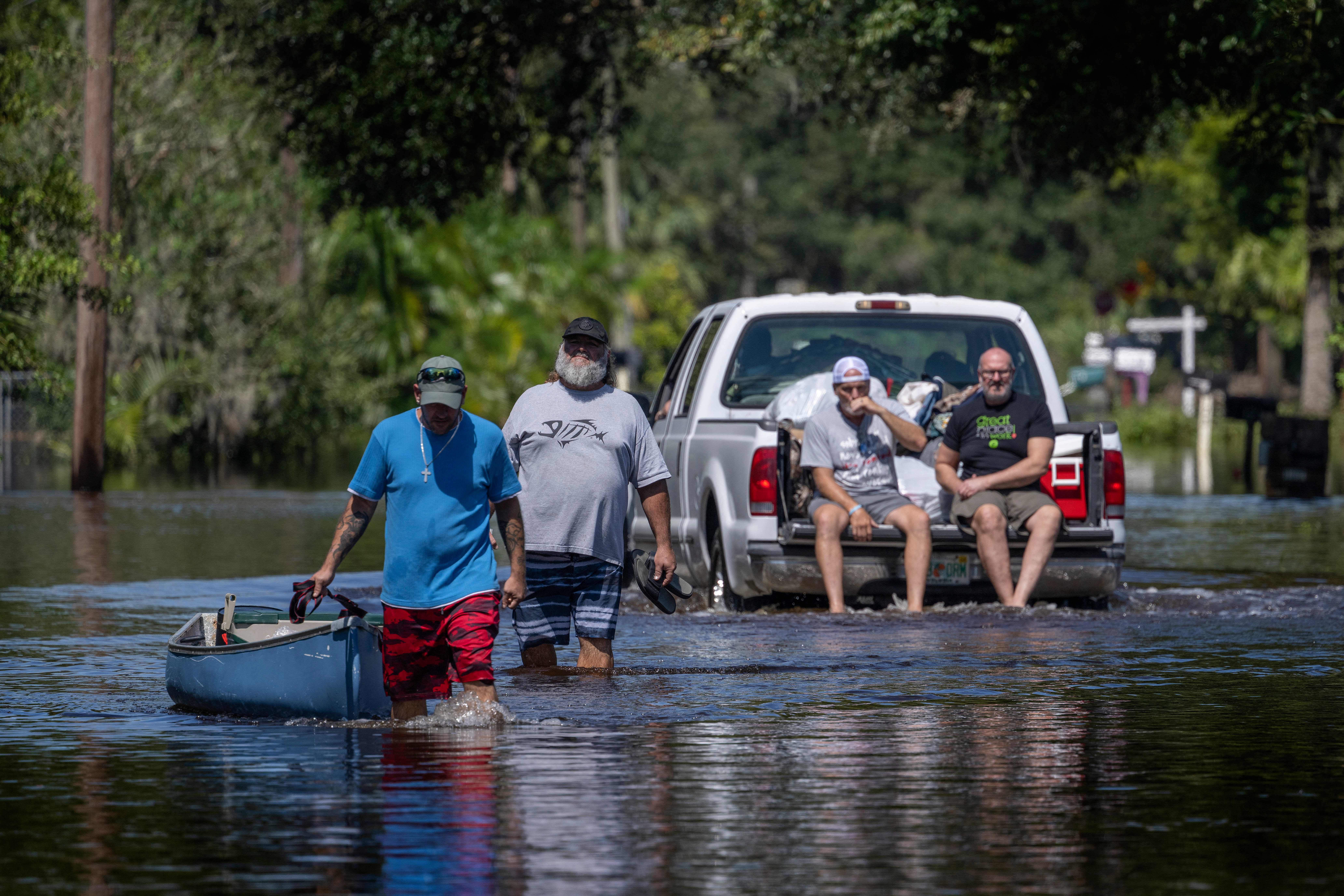 A man tows a canoe through a flooded street of his neighborhood as a truck passes in New Smyrna Beach, Florida, on Sept. 30, 2022, after Hurricane Ian slammed the area. Credit: Jim Watson/AFP via Getty Images