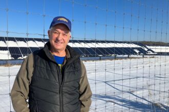 Ed Eichten stands next to a solar array on his farm near Center City, Minnesota. Credit: Dan Gearino