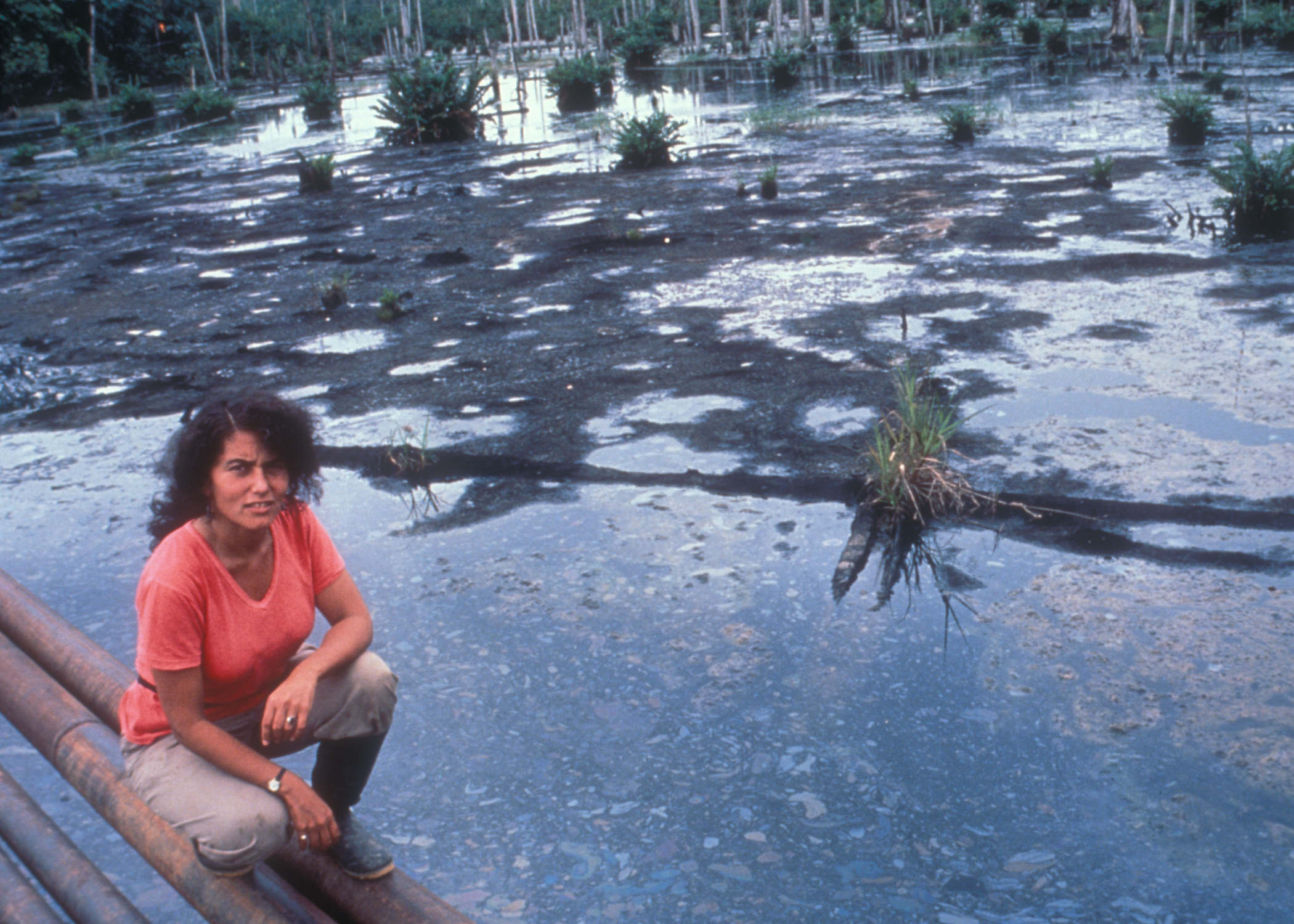 Judith Kimerling kneeling on pipelines above a drilling waste pit in the Ecuadorian Amazon in July 1990. Credit: Courtesy of Judith Kimerling