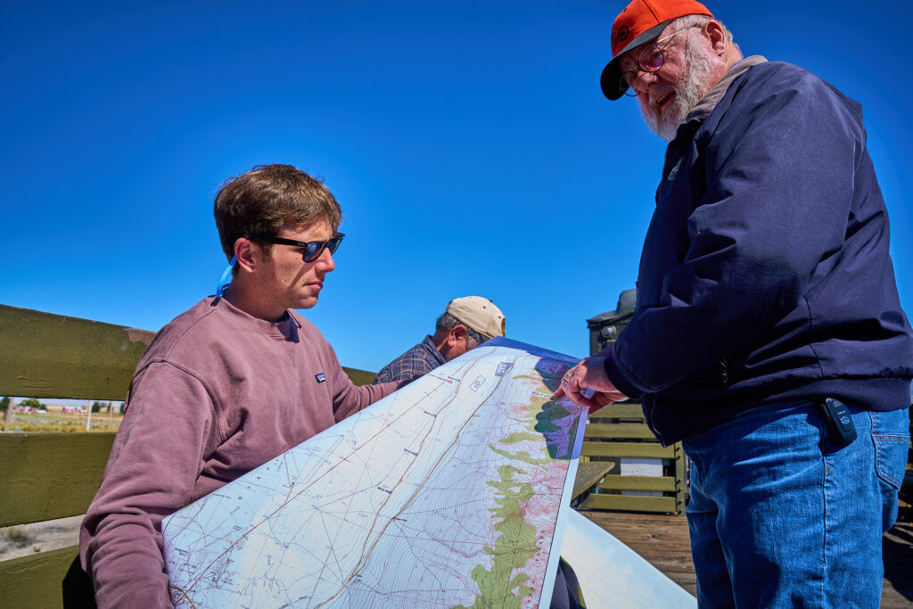 Kyle Roerink, left, and  Mark Bassett, right, look over a topographical map of the land around Ely, Nevada, with the drill site for the White Pines Pump Storage project while riding one of the Nevada Northern Railway Trains out toward the area on Thursday Oct. 5, 2023. Credit: Alex Gould