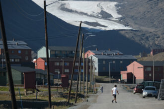A man wearing shorts and a t-shirt walks in the town center as the melting Longyear glacier looms behind during a summer heat wave on Svalbard archipelago on July 30, 2020 in Longyearbyen, Norway. Credit: Sean Gallup/Getty Images