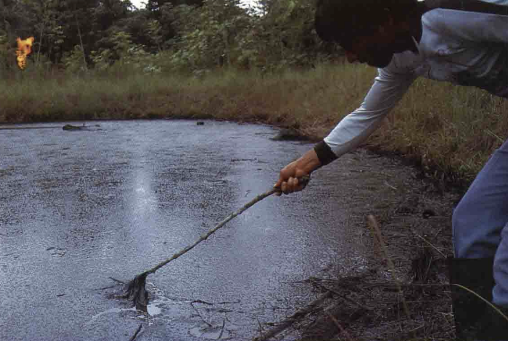 A man moves a branch through toxic drilling wastes dumped in the Ecuadorian Amazon rainforest. Photo originally published in Amazon Crude. Photo originally published in Kimerling's Amazon Crude. Credit: courtesy of Judith Kimerling